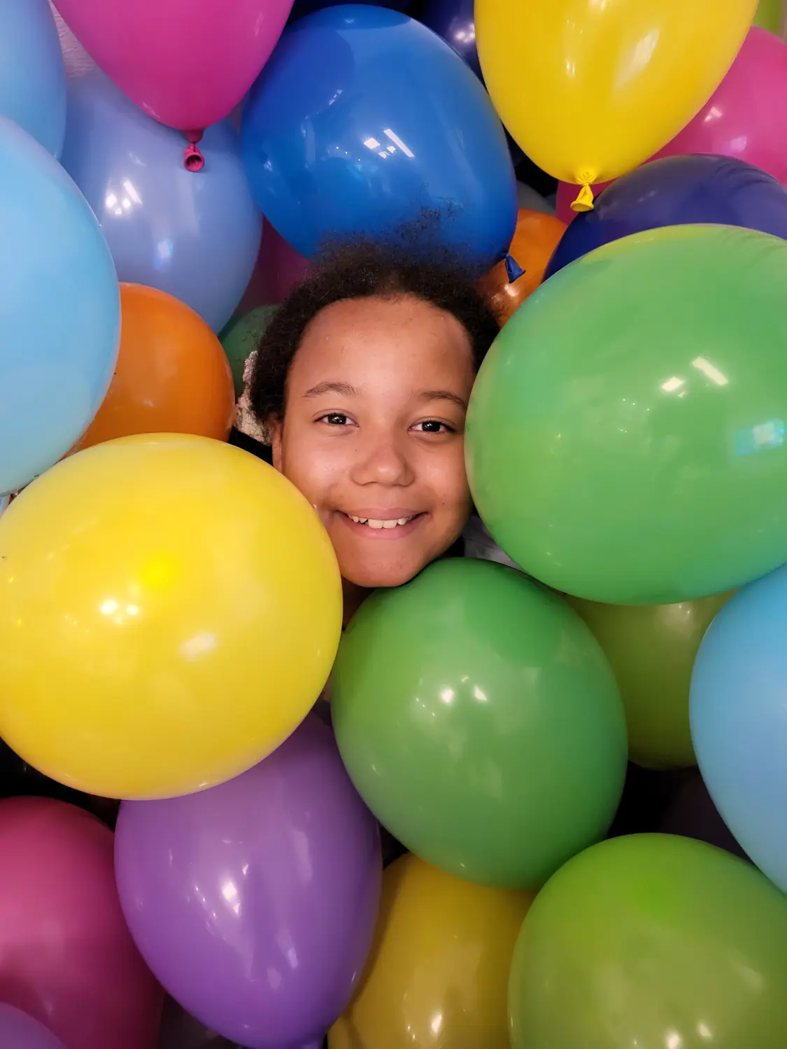 Fröhliches Mädchen, das durch Luftballons späht